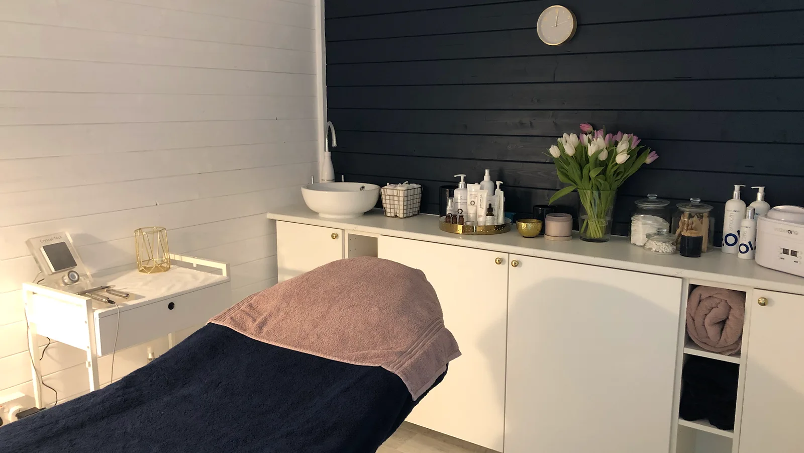 The clinic's treatment room, with a treatment bed, flowers and a navy feature wall