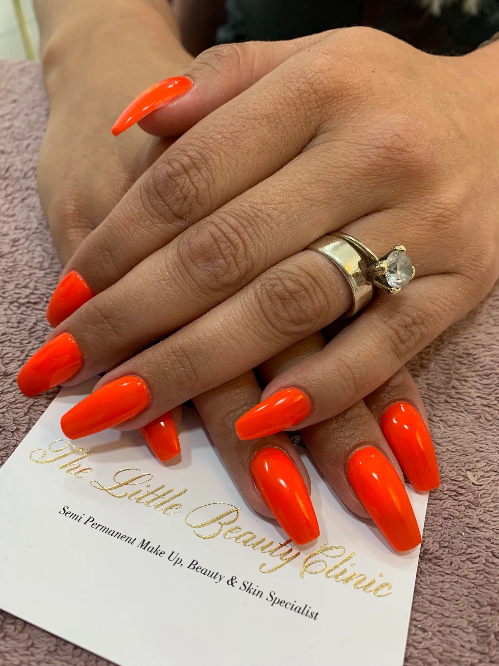 Vivid orange nails with The Little Beauty Clinic's business card